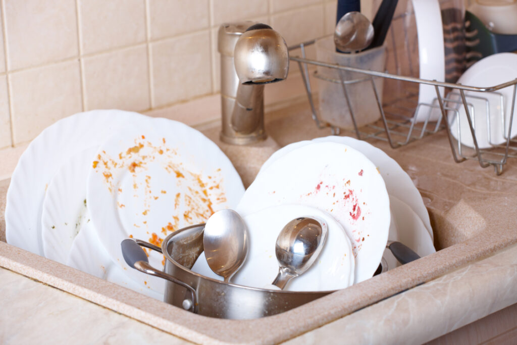 Pile of dirty dishes like plates, pot and cutlery in the sink